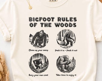 Może przedstawiać: Kremowy t-shirt z krótkim rękawem z napisem "BIGFOOT RULES OF THE WOODS" oraz czterema okrągłymi ilustracjami przedstawiającymi Bigfoot wykonującego różne zajęcia na świeżym powietrzu z podpisami: "Clean up your camp", "Pack it in - Pack it out", "Bury your own scat" oraz "Take time to enjoy it".