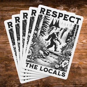 May include: A stack of rectangular stickers featuring a black and white illustration of a Bigfoot creature walking through a forest near a waterfall. The text "RESPECT" is printed at the top and "THE LOCALS" is printed at the bottom of each sticker.