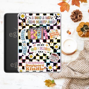 Op de afbeelding: Een zwarte Kindle-hoes met een doorzichtige hoes met een kleurrijk ontwerp. Het ontwerp omvat een geruite achtergrond, boeken, bloemen, bliksemschichten en tekst met de tekst "A Book a Day Keeps Reality Away" en "Emotional Support Kindle."