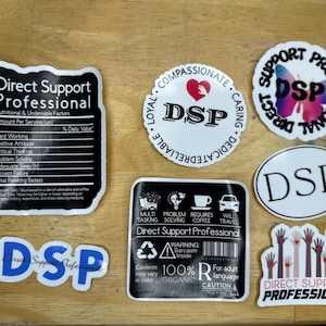 May include: A collection of white stickers with black text and graphics. The stickers have various designs, including a nutrition facts label, a circle with "DSP" and a heart, and a butterfly. The stickers are for Direct Support Professionals.