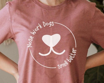 May include: A heather mauve t-shirt with a white graphic of a dog's nose and the text "Nose Work Dogs Smell Better".
