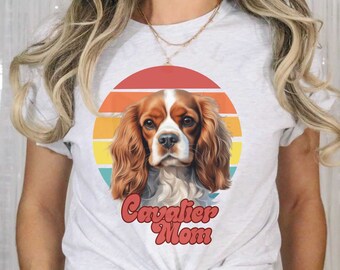 Puede incluir: Camiseta blanca con un gráfico de puesta de sol retro con un perro Cavalier King Charles Spaniel. El texto "Cavalier Mom" está impreso debajo del perro.