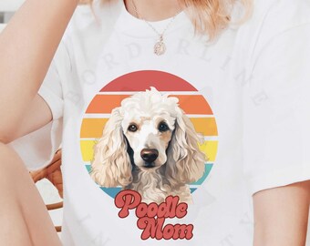 May include: White t-shirt featuring a poodle illustration within a retro sunset design. The graphic includes the text "Poodle Mom" in a playful font. The shirt also has the word "white" printed on the bottom left.