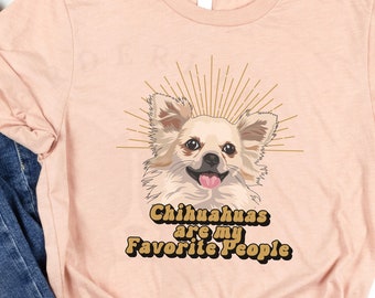 May include: A peach colored t-shirt with a chihuahua illustration and the text "Chihuahuas are my Favorite People" in a retro font. The shirt is laid out on a white surface with a pair of blue jeans.