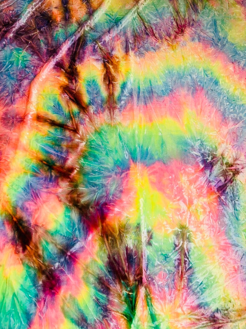 May include: A vibrant tie-dye textile featuring a swirling pattern of rainbow colors. The design includes shades of yellow, green, blue, pink, and brown, creating a psychedelic and artistic effect. The fabric appears textured and crinkled.