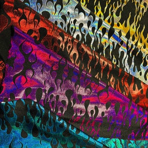 May include: Close-up of several fabric samples with a flame pattern. The fabrics display a variety of colors, including red, silver, gold, purple, and teal, all with a black background. The flame design is consistent across all samples.