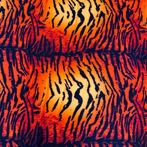 Puede incluir: Un textil vibrante con un estampado de rayas de tigre. El dise&ntilde;o presenta rayas negras sobre un degradado de tonos naranja y amarillo, creando un efecto visual audaz y llamativo.