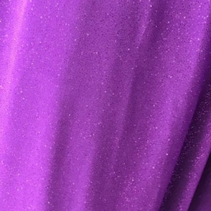 May include: Purple fabric with a sparkly, glittery texture. The fabric has a slight sheen and is soft to the touch.