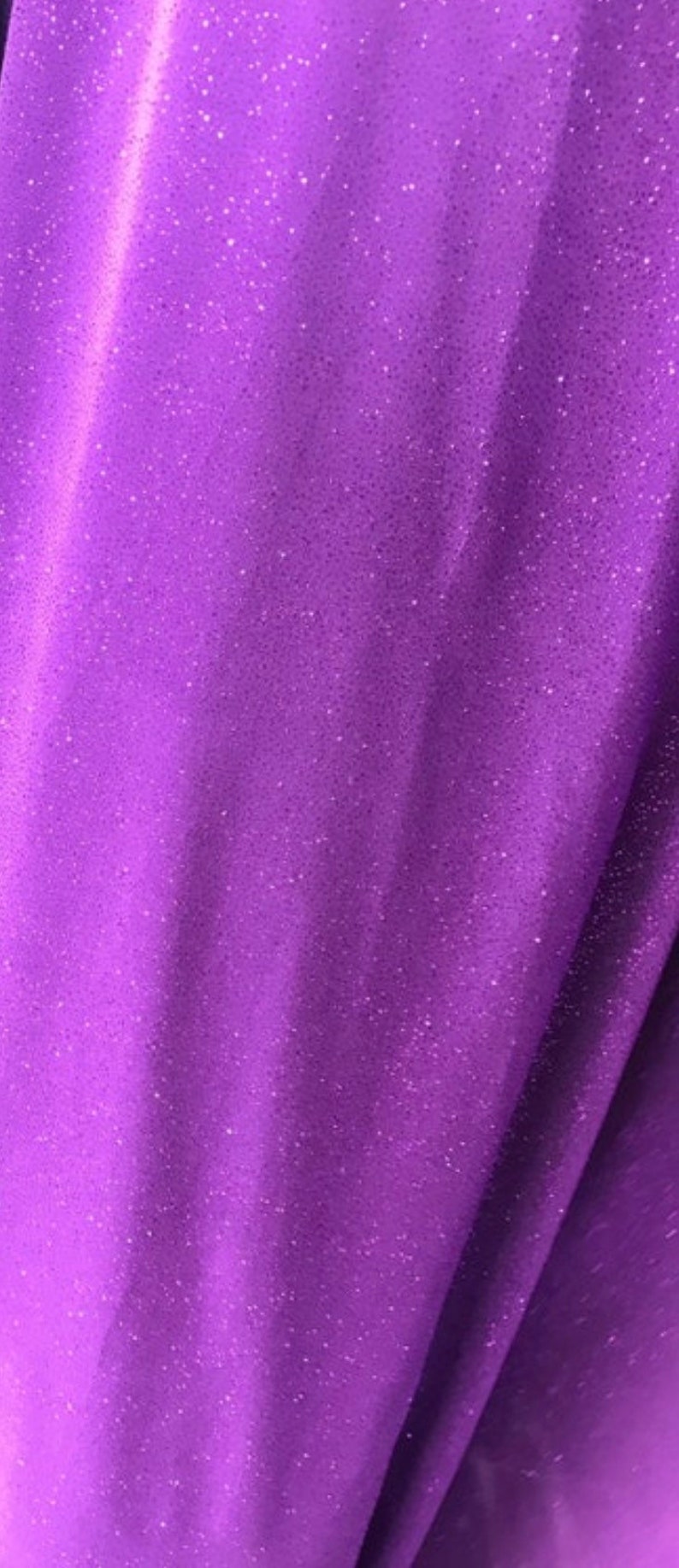 May include: Purple fabric with a sparkly, glittery texture. The fabric has a slight sheen and is soft to the touch.