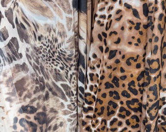 May include: Close-up of three different fabrics with animal print patterns. The fabrics feature shades of brown, tan, and black, with varying patterns resembling leopard and giraffe prints. The fabrics are draped, creating folds and shadows.