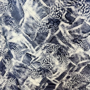 Op de afbeelding: Abstract stoffen ontwerp met een witte achtergrond en een patroon van blauwe denim patches en witte en grijze swirls.