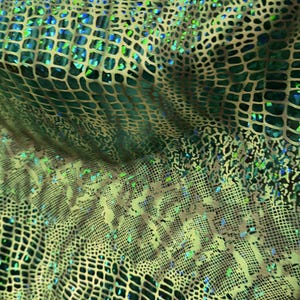 May include: A fabric featuring a repeating reptilian scale pattern in shades of metallic green, gold, and black. The surface has a reflective, iridescent quality with small, shimmering blue and green highlights embedded within the textured grid.