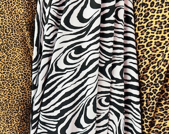 May include: Close-up of three fabric patterns: leopard print in brown and black, zebra stripes in black and white, and another leopard print. The fabrics are draped, showcasing the textures and designs.