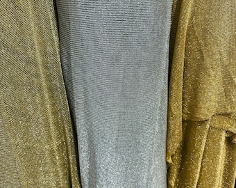 May include: A roll of silver metallic fabric positioned between two layers of gold metallic fabric. The material features a fine, semi-sheer, knit-like texture with a consistent shimmering finish across the entire surface of the textile.