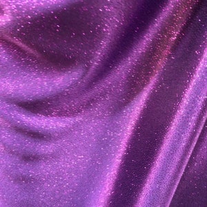 May include: Purple fabric with a sparkly, iridescent finish. The fabric has a subtle texture and a soft, flowing drape.