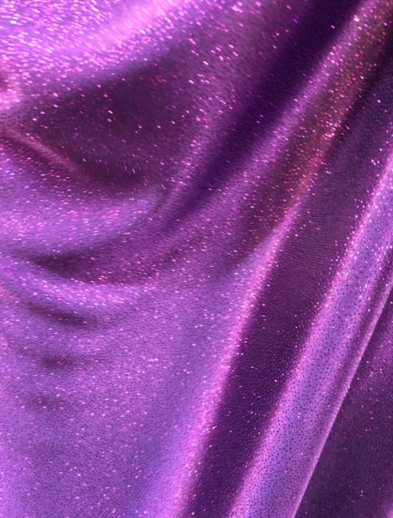 May include: Purple fabric with a sparkly, iridescent finish. The fabric has a subtle texture and a soft, flowing drape.