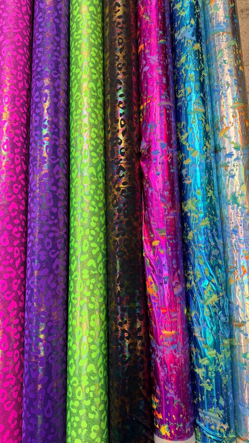 Puede incluir: Varios rollos de tela en colores vibrantes. Las telas presentan estampados de leopardo en tonos rosa, morado, verde y negro. Otras telas tienen un dise&ntilde;o de salpicaduras en tonos rosa, azul y dorado.