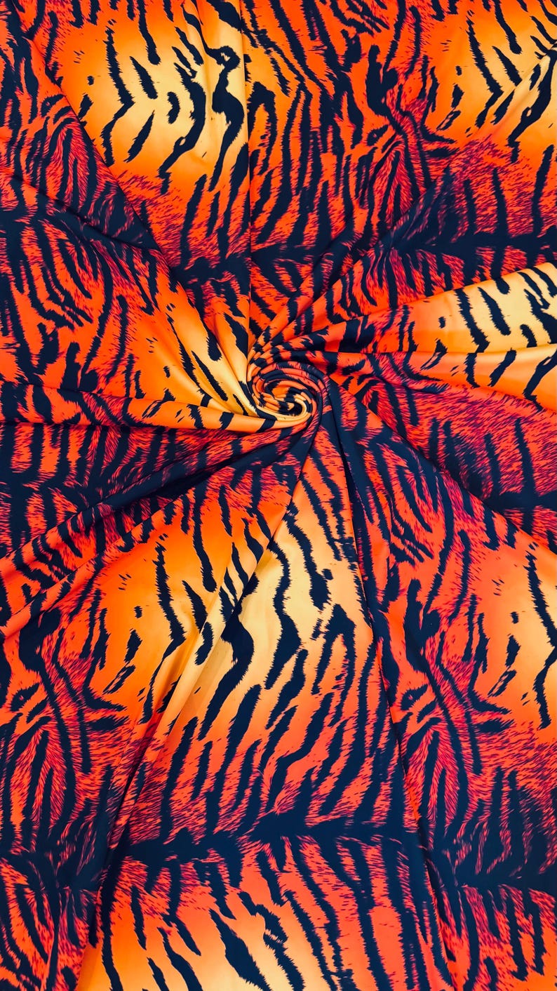 Puede incluir: Primer plano de una tela con un estampado de rayas de tigre. La tela presenta una mezcla de colores naranja, rojo y negro, creando un dise&ntilde;o llamativo. El material est&aacute; recogido en el centro, mostrando su textura y ca&iacute;da.