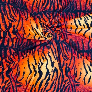 Puede incluir: Una tela vibrante con un estampado de rayas de tigre. El dise&ntilde;o presenta tonos naranja y amarillo con rayas azul marino oscuro. La tela est&aacute; reunida en espiral, mostrando el flujo y la textura del patr&oacute;n.