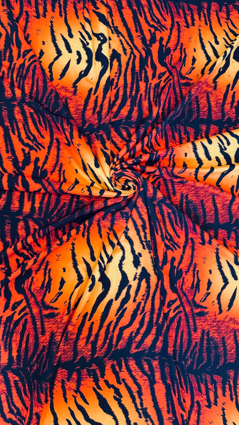 Puede incluir: Una tela vibrante con un estampado de rayas de tigre. El dise&ntilde;o presenta tonos naranja y amarillo con rayas azul marino oscuro. La tela est&aacute; reunida en espiral, mostrando el flujo y la textura del patr&oacute;n.