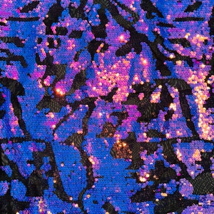 May include: Close-up of iridescent blue and purple sequins on a black mesh fabric. The sequins are arranged in a swirling pattern.