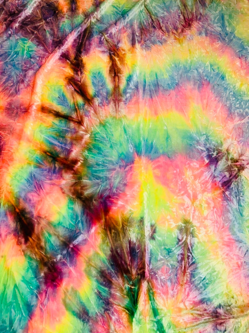 May include: A vibrant tie-dye textile with a spiral pattern. The fabric features a blend of colors, including shades of yellow, pink, green, blue, and brown. The design has a textured appearance, with visible folds and creases in the material.