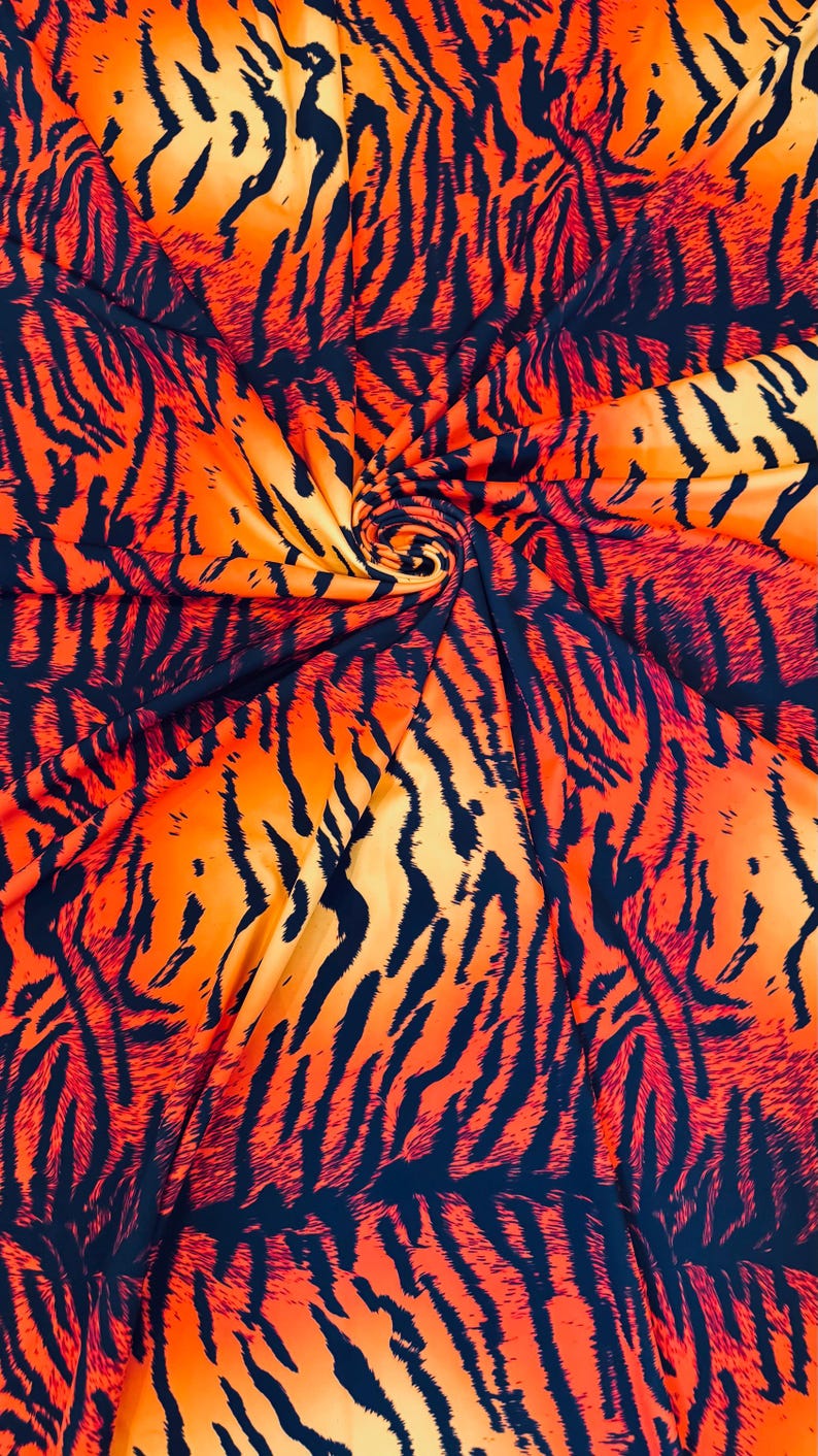 Puede incluir: Primer plano de una tela con un estampado de rayas de tigre. La tela presenta audaces rayas naranjas y negras, creando un efecto visual llamativo. El material est&aacute; recogido en un remolino, mostrando el flujo del patr&oacute;n.