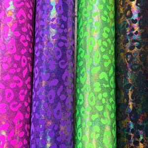 Puede incluir: Cuatro rollos de tela con un dise&ntilde;o de estampado de leopardo. Los rollos son en tonos de rosa, morado, verde y negro. La tela tiene un acabado brillante y hologr&aacute;fico.