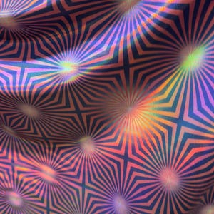 May include: Close-up of a fabric with a repeating geometric pattern. The design features radiating lines and starburst shapes in shades of blue, pink, and orange. The fabric has a shimmering, iridescent quality.