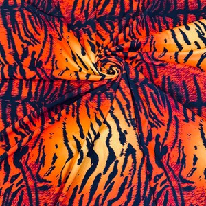 Puede incluir: Tela naranja vibrante con un patr&oacute;n de rayas de tigre en negro. La tela est&aacute; doblada y arremolinada, creando una textura visual din&aacute;mica. Los colores llamativos y el patr&oacute;n sugieren un tema salvaje y animal.