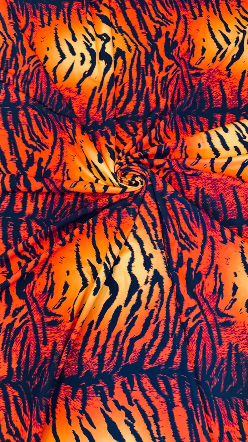 Puede incluir: Tela naranja vibrante con un patr&oacute;n de rayas de tigre en negro. La tela est&aacute; doblada y arremolinada, creando una textura visual din&aacute;mica. Los colores llamativos y el patr&oacute;n sugieren un tema salvaje y animal.