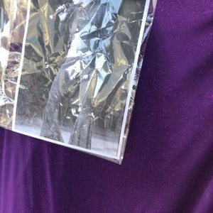 May include: A close-up of a purple sparkly fabric with a black and white photo of a person singing into a microphone. The photo is in a clear plastic sleeve.