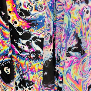 Puede incluir: Primer plano de una tela negra con un patr&oacute;n de espiral psicod&eacute;lico colorido. El patr&oacute;n se asemeja a las manchas de aceite con colores iridiscentes como el azul, el verde, el amarillo, el rosa y el morado.