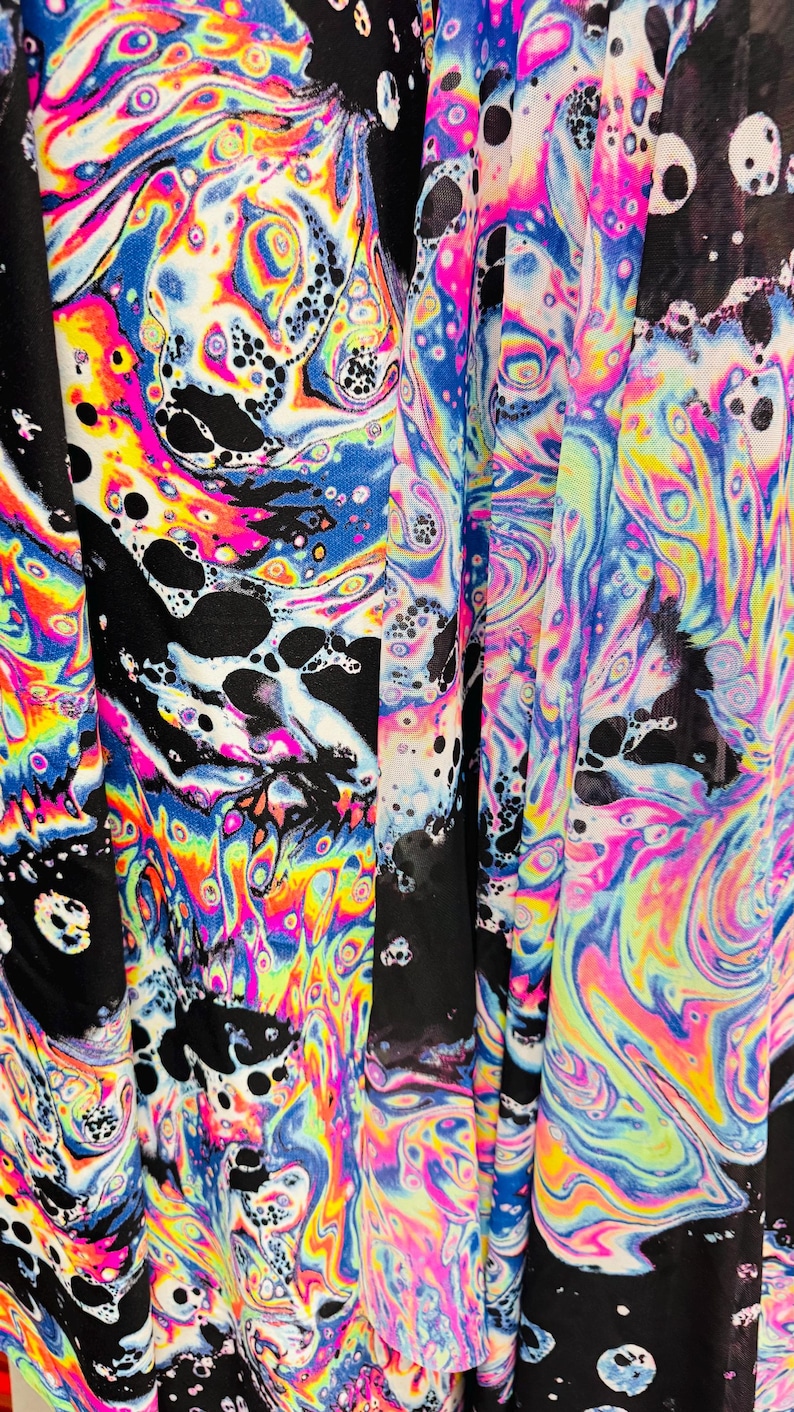 Puede incluir: Primer plano de una tela negra con un patr&oacute;n de espiral psicod&eacute;lico colorido. El patr&oacute;n se asemeja a las manchas de aceite con colores iridiscentes como el azul, el verde, el amarillo, el rosa y el morado.