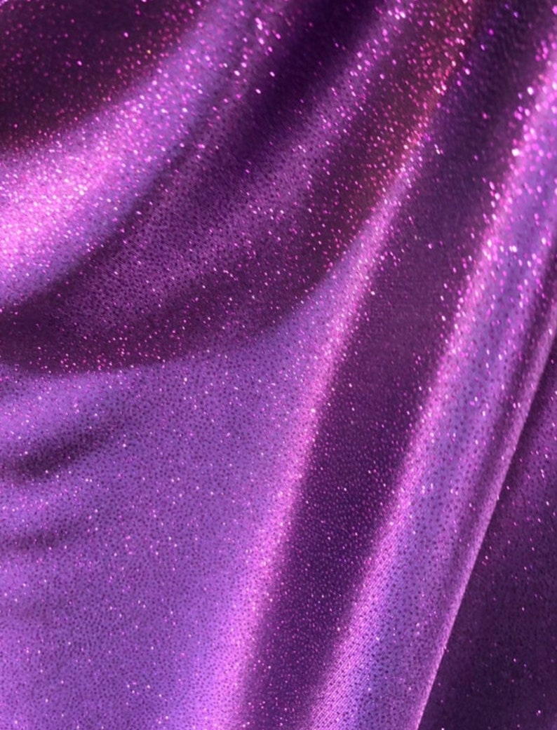 May include: Purple fabric with a sparkly, glittery texture. The fabric is smooth and has a slight sheen.