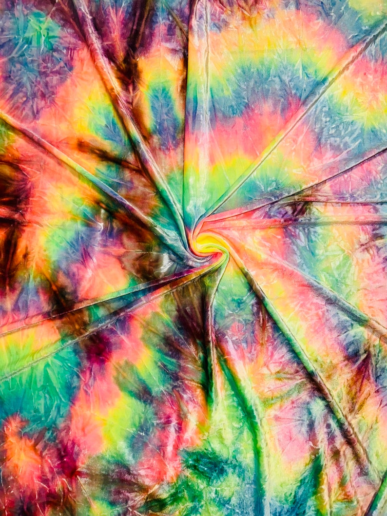 May include: A vibrant tie-dye fabric with a swirling pattern. The colors include shades of pink, yellow, green, blue, and brown. The fabric is folded and gathered in the center, creating a spiral effect. The overall effect is bright and colorful.