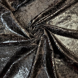 Puede incluir: Una tela de color marrón oscuro y negro con un patrón de piel de serpiente brillante en relieve. El material está fruncido en el centro, creando pliegues profundos y reflejos que resaltan el diseño texturizado de escamas inspirado en reptiles.