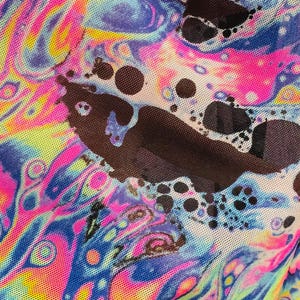 Puede incluir: Primer plano de una tela colorida con un patr&oacute;n abstracto en espiral en tonos de rosa, azul, amarillo y verde. La tela tiene una textura de malla y est&aacute; superpuesta con puntos negros.
