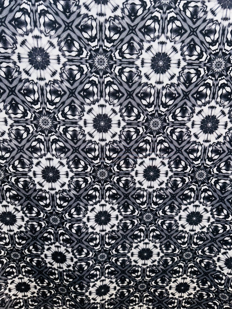May include: Black and white fabric with a repeating geometric pattern of stars and diamonds. The fabric has a soft, flowing texture.