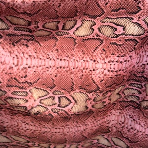 May include: Close-up of a pink snakeskin pattern. The fabric features a repeating design of scales in shades of pink, brown, and beige, creating a textured appearance. The pattern is detailed and realistic.