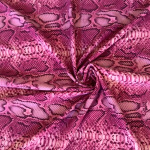May include: A fabric featuring a vibrant pink and magenta snakeskin pattern. The material is gathered in the centre, creating folds that highlight the repeating scale-like texture and the varying shades of deep purple and light pink throughout.