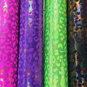 Puede incluir: Cuatro rollos de tela estampada en colores vibrantes. Los rollos muestran un dise&ntilde;o de estampado de leopardo en tonos de rosa, morado, verde y negro. La tela tiene un acabado brillante y hologr&aacute;fico.