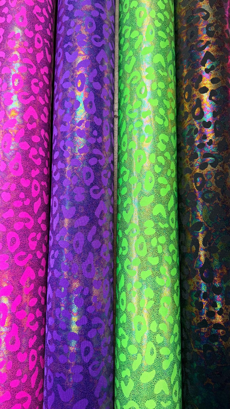 Puede incluir: Cuatro rollos de tela estampada en colores vibrantes. Los rollos muestran un dise&ntilde;o de estampado de leopardo en tonos de rosa, morado, verde y negro. La tela tiene un acabado brillante y hologr&aacute;fico.