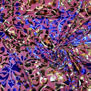 May include: Close-up of a burgundy fabric with a swirling pattern. The design features blue, gold, and black floral and abstract shapes. The fabric has a velvet-like texture, with a slight sheen.