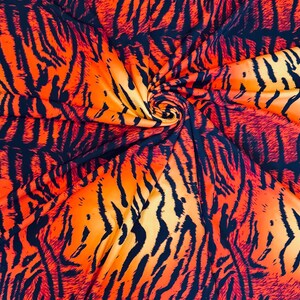 Puede incluir: Primer plano de una tela con un vibrante estampado de rayas de tigre. La tela presenta una mezcla de colores naranja, amarillo y negro, creando un dise&ntilde;o audaz y llamativo. La tela se utiliza probablemente para ropa o decoraci&oacute;n del hogar.