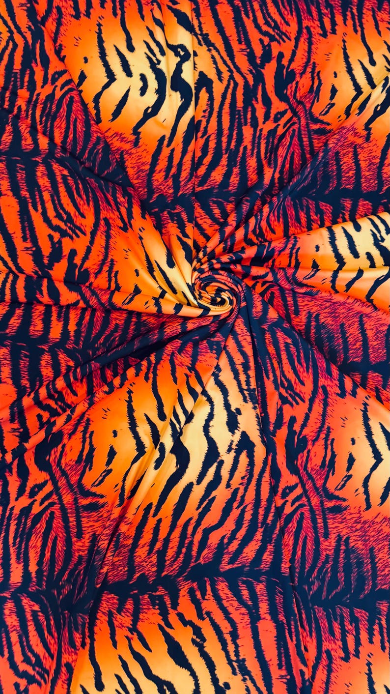 Puede incluir: Primer plano de una tela con un vibrante estampado de rayas de tigre. La tela presenta una mezcla de colores naranja, amarillo y negro, creando un dise&ntilde;o audaz y llamativo. La tela se utiliza probablemente para ropa o decoraci&oacute;n del hogar.
