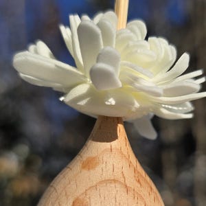 May include: A small, clear glass bottle with a wooden top and a white flower on top. The bottle is filled with a yellow liquid and glitter.