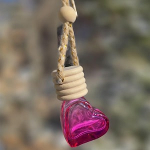 May include: A pink heart-shaped glass bottle with a wooden cap and a beige rope hanging from it.