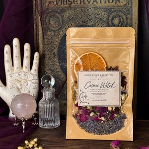 May include: A brown paper pouch containing a dried botanical blend with a label reading Cosmic Witch, Good Witch Bad Witch, Crafting Intentions. The blend includes dried orange slices, star anise, rose buds, and lavender. The pouch is sealed at the top.