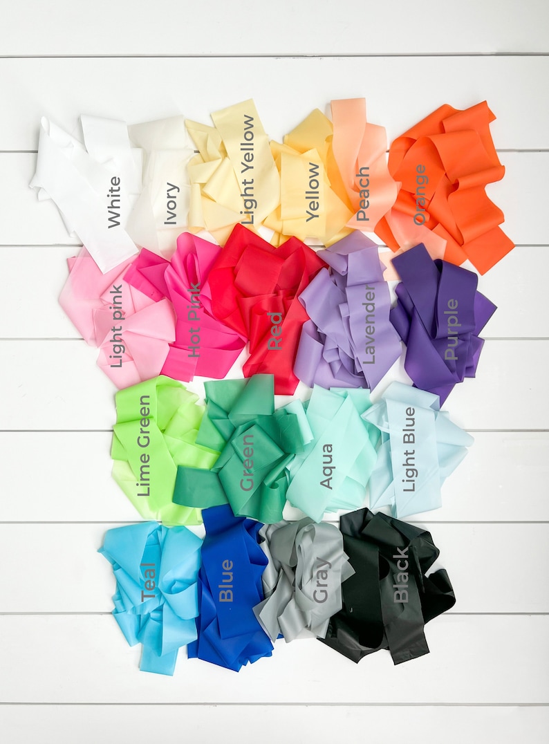 May include: A collection of 18 different coloured fabric ribbons, each with a label identifying its colour. The colours include white, ivory, light yellow, yellow, peach, orange, light pink, hot pink, red, lavender, purple, lime green, green, aqua, light blue, teal, blue, grey, and black.
